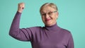 Funny elegant elderly woman in glasses purple turtleneck showing her muscles