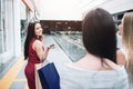 Cheerful and beautiful girl in red dress is looking back to her friends and smiling. Also she holds two bags and phone Royalty Free Stock Photo