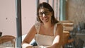 Cheerful, beautiful hispanic woman enjoying a cup of hot caffeine-filled coffee in a sunny cafe, her smile radiant as she relaxes