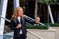 Cheerful beautiful student girl has online video conversation on smart phone on the street, enjoying walk outdoors. Royalty Free Stock Photo