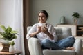 Cheerful beautiful young Indian woman holding cell, sitting in armchair Royalty Free Stock Photo