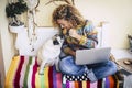 Cheerful beautiful young woman share a cookie with her funny and lovely pug dog while work with laptop computer at home on a