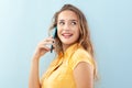 Cheerful and beautiful young woman talking on cell phone, with long hair wearing a yellow blouse. Isolated on light blue Royalty Free Stock Photo