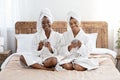 Cheerful besties in bathrobes sitting on bed, smiling at camera Royalty Free Stock Photo