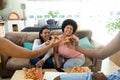 Cheerful biracial friends raising toast with pizza slices while spending leisure time in living room Royalty Free Stock Photo