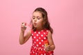 Cheerful Birthday baby girl in stylish pink dress blowing soap bubbles, isolated over pink background with copy space. Gorgeous Royalty Free Stock Photo