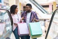 Cheerful Black Couple Chatting While Riding Escalator In Department Store, Shopping Together Royalty Free Stock Photo