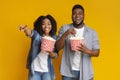 Cheerful black couple eating popcorn from buckets and laughing at camera Royalty Free Stock Photo