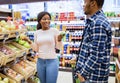 Cheerful black couple having fun shopping together, choosing healthy food at fruits and veggies section of huge mall Royalty Free Stock Photo