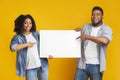 Cheerful black couple holding and pointing at blank advertisement placard