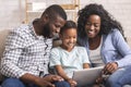 Cheerful black family using digital tablet together at home