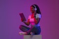 Cheerful Black Female Sitting In Neon Light And Using Digital Tablet Royalty Free Stock Photo