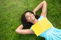 Joyful black girl with notebook lying on green grass at park, empty space