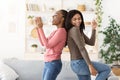 Cheerful black girlfriends singing and dancing at home