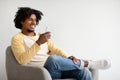 Cheerful Black Guy Relaxing With Smartphone In Armchair At Home Royalty Free Stock Photo