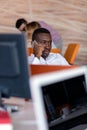 Cheerful black guy is watching at his laptop screen, at his work place, with arms behind the head. Royalty Free Stock Photo