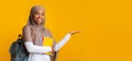 Cheerful black islamic female student in hijab pointing aside with hand