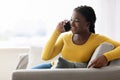 Cheerful Black Lady Talking On Cellphone While Relaxing On Couch At Home