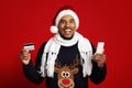 Cheerful black man with smartphone and credit card celebrating xmas