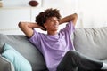 Cheerful black teenager relaxing on comfy couch at home during covid quarantine Royalty Free Stock Photo