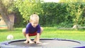 Cheerful blond boy jumping on trampoline in the summer garden