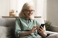 Cheerful blonde old retired woman in glasses using mobile phone Royalty Free Stock Photo