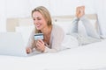 Cheerful blonde shopping online on the bed