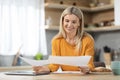 Cheerful blonde woman entrepreneur working from home, reading papers Royalty Free Stock Photo