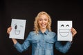 Blonde woman holding papers with happy faces isolated on black Royalty Free Stock Photo