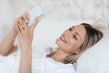 Cheerful blonde woman resting in bed with cell phone Royalty Free Stock Photo