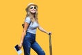 Cheerful blonde woman in sunglasses posing with baggage and holding passport with tickets over yellow background. Royalty Free Stock Photo