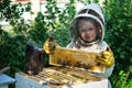 Cheerful boy beekeeper in protective suit near beehive. Honeycomb with honey. Organic food concept. The most useful