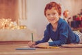 Cheerful boy drawing with pencils while lying on floor