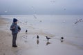 A cheerful boy feeds gulls on the seashore in winter, spring or autumn. many gulls are flying around. Cold day by the sea. Royalty Free Stock Photo