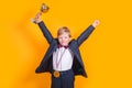 Cheerful boy holding a golden trophy and gold medal on yellow background