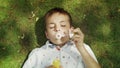 Cheerful boy lying on green grass. Adorable child blowing soap bubbles at camera Royalty Free Stock Photo