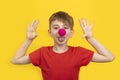 Cheerful boy with red clown nose and red t-shirt on yellow background. 1 April Fools day concept Royalty Free Stock Photo