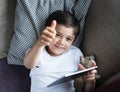 Cheerful boy showing thumb up, Top view portrait child playing game or watching cartoon on tablet, Happy kid lying on sofa looking Royalty Free Stock Photo