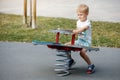 The cheerful boy springs up and balances on the swings of a modern outdoor playground