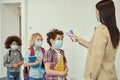 Cheerful boy wearing face mask watching his teacher measuring temperature, screening kid with digital thermometer while Royalty Free Stock Photo