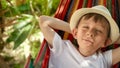 A cheerful boy, wearing a sunny smile, swings and lounges in a garden hammock, embodying the spirit of summertime