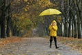 Cheerful boy in a yellow raincoat is jumping in the park with an umbrella. Autumn rainy day