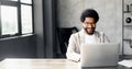 A cheerful Brazilian businessman in a smart casual beige suit in loft office using laptop