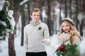 Cheerful bride and groom in beige knitted pullovers are walking in snowy forest. Selective focus on the groom. Artwork