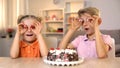 Cheerful brother and sister holding cake cherries front eyes, playing together