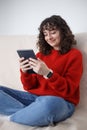 Happy Ukrainian girl reads ebook on tablet computer. Cheerful curly female person sitting on sofa at home and browsing internet on Royalty Free Stock Photo