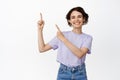 Cheerful brunette girl pointing fingers at upper left corner and smiling proud, showing advertisement, company info Royalty Free Stock Photo