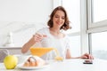 Cheerful brunette girl pouring juice into glass while sitting an