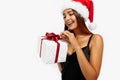 Cheerful attractive brunette in a red Christmas hat and black dress, holding a gift box on a white background, Concept of Royalty Free Stock Photo