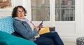Cheerful brunette senior woman using smartphone while sitting on sofa Royalty Free Stock Photo